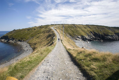 Wide angle shot of a person walking alone on a dirt road by sea against sky.