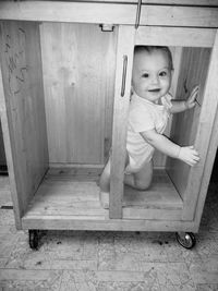 Portrait of cute baby boy in wooden cabinet at home