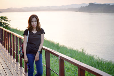 Portrait of young woman standing by railing against sea