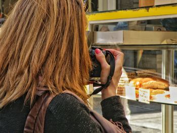 Rear view of woman photographing display cabinet