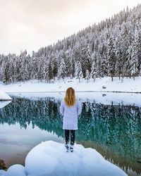 Rear view of woman standing on snow by lake in forest during winter