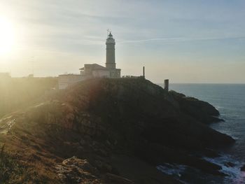 Lighthouse amidst sea and buildings against sky