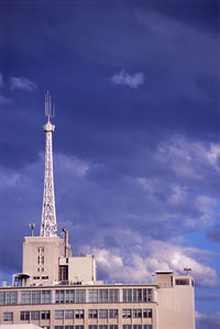 Radio tower on building against cloudy sky