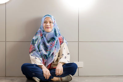 Portrait of smiling young woman wearing hijab sitting on tiled floor