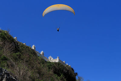 Low angle view of person paragliding against clear blue sky