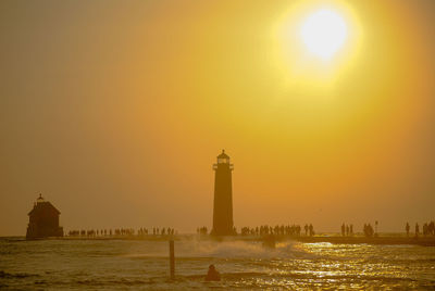 Lighthouse by building against sky during sunset