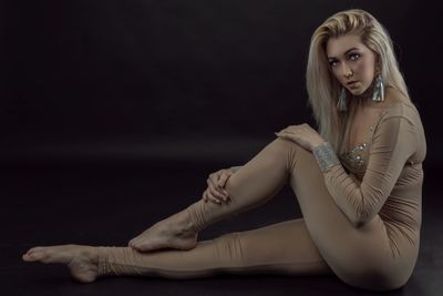 Portrait of young woman sitting against black background