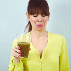 Woman having drink while standing against wall