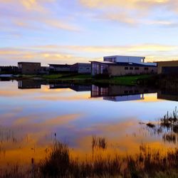 Buildings by lake against sky during sunset