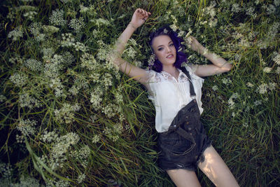 Portrait of a teenage girl with purple hair and an earring in her nose lying in the grass in nature