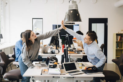 Happy male and female computer programmers doing high-five over computer at desk in creative office