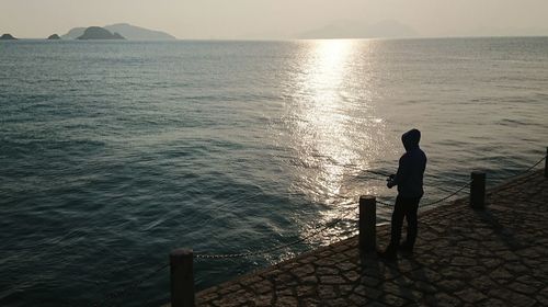 Silhouette man standing on pier by sea against sky during sunset