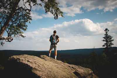 Man standing on top of a rock looking down into a valley in zdarske vrchy in the czech republic