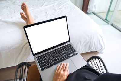 Mockup image of a woman using and typing on laptop with blank white desktop screen in bedroom