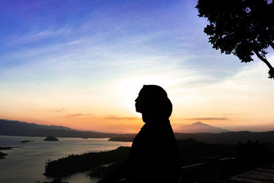 Silhouette woman standing by sea against sky during sunset