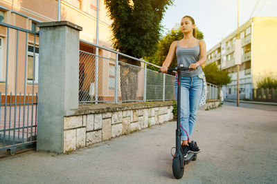 Young woman standing on electric push scooter on street