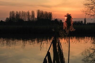 Silhouette trees by lake against sky during sunset