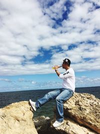 Man sitting on rock by sea against sky