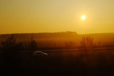 Car on landscape against sky during sunset