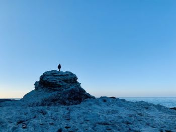 Man standing on rock by sea against clear blue sky at dawn