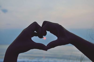 Close-up of hand holding heart shape against sea