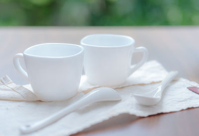 Close-up of cups with spoons and napkin on table