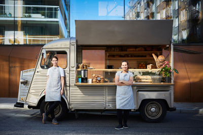 Full length portrait of confident female owners standing outside foot truck parked on city street