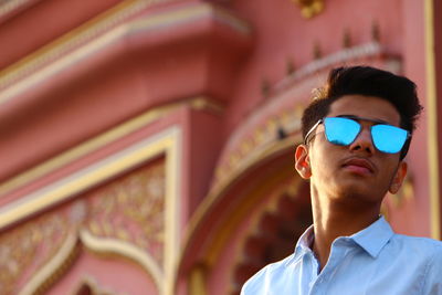 Low angle view of young man wearing sunglasses standing against building