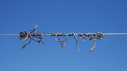 Low angle view of barbed wire against clear blue sky