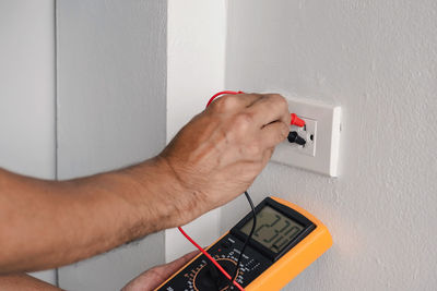 Electrician is using a digital meter to measure the voltage at the power outlet in on the wall.