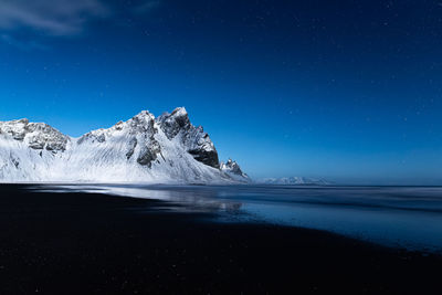 Snowy peaks lit by full moon light on a lonely calm clear blue night at stokksnes beach in iceland