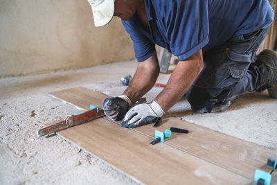 Male manual worker installing parquet flooring in house