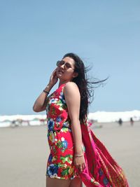 Side view of young woman standing at beach against clear sky during sunny day