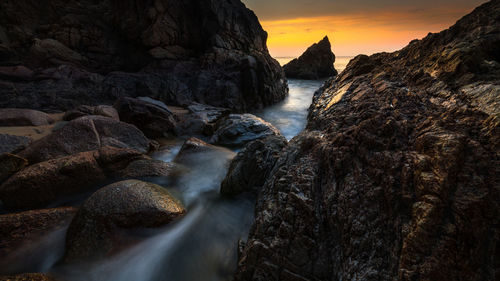 Rocks in sea against sky during sunset