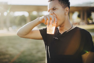 Thoughtful young man drinking alcohol while looking away on sunny day