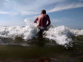 Rear view of shirtless man enjoying waves in sea against sky