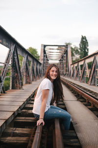 Portrait of smiling young woman on footbridge against sky