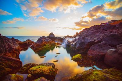 Rocks on shore against sky during sunset