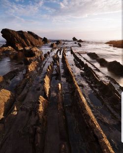 Panoramic view of rocks on beach against sky during sunset