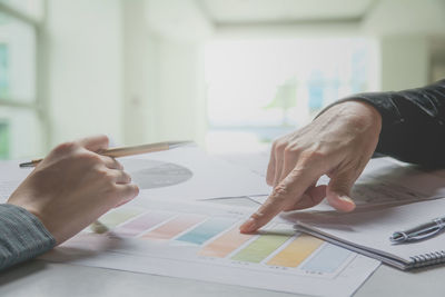 Cropped hands of business people discussing graphs at desk in office