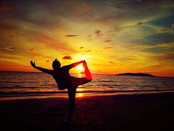 Silhouette of woman jumping in sea at sunset