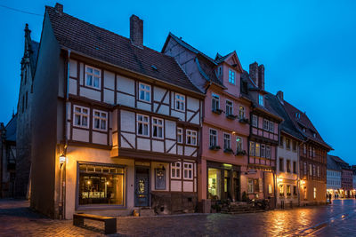 Illuminated buildings by street against sky at dusk