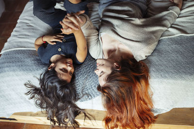 Smiling mother and daughter holding hands while lying on bed at home