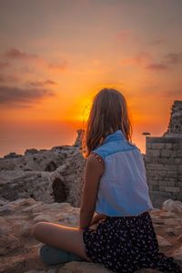 Rear view of woman standing on rock against sky during sunset