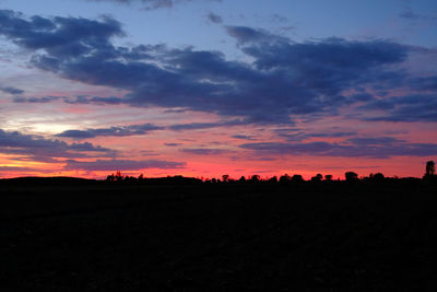 Silhouette trees on field against dramatic sky during sunset