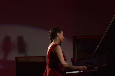 Side view of woman playing piano against wall at home