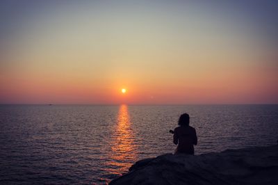 Man looking at sea against sky during sunset