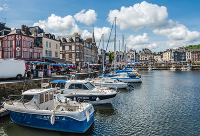 Sailboats moored on harbor by buildings in city against sky