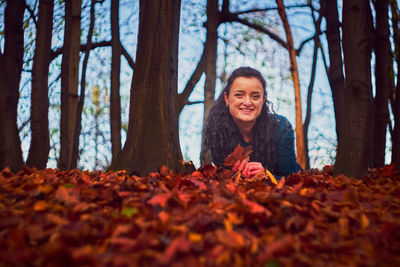 Portrait of smiling young woman with autumn leaves in forest