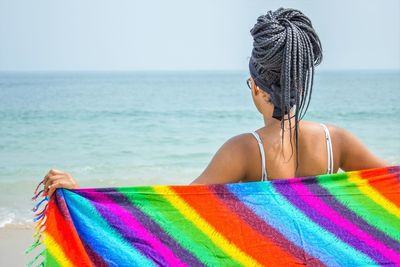 Rear view of woman with multi colored sarong at beach against sky